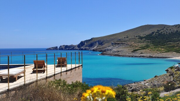 Une terrasse dotée de chaises en bois, offrant une vue sur une mer turquoise et un paysage montagneux.