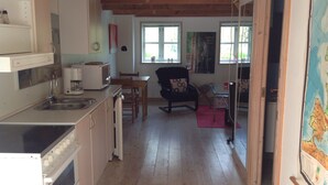A kitchen with a stove, sink, and coffee maker, a dining area with a table and chairs, and a large window with a view of the outdoors.