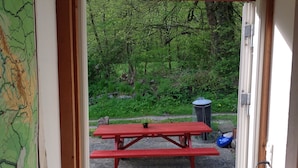 A red picnic table in an outdoor area with a map on the wall, a trash can, and a blue object on the ground.