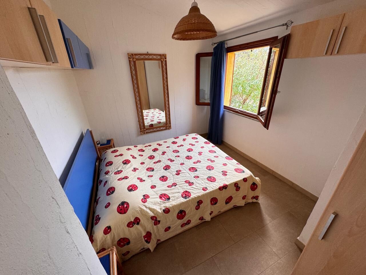 A small bedroom with a bed, a window, a mirror, and a wardrobe.