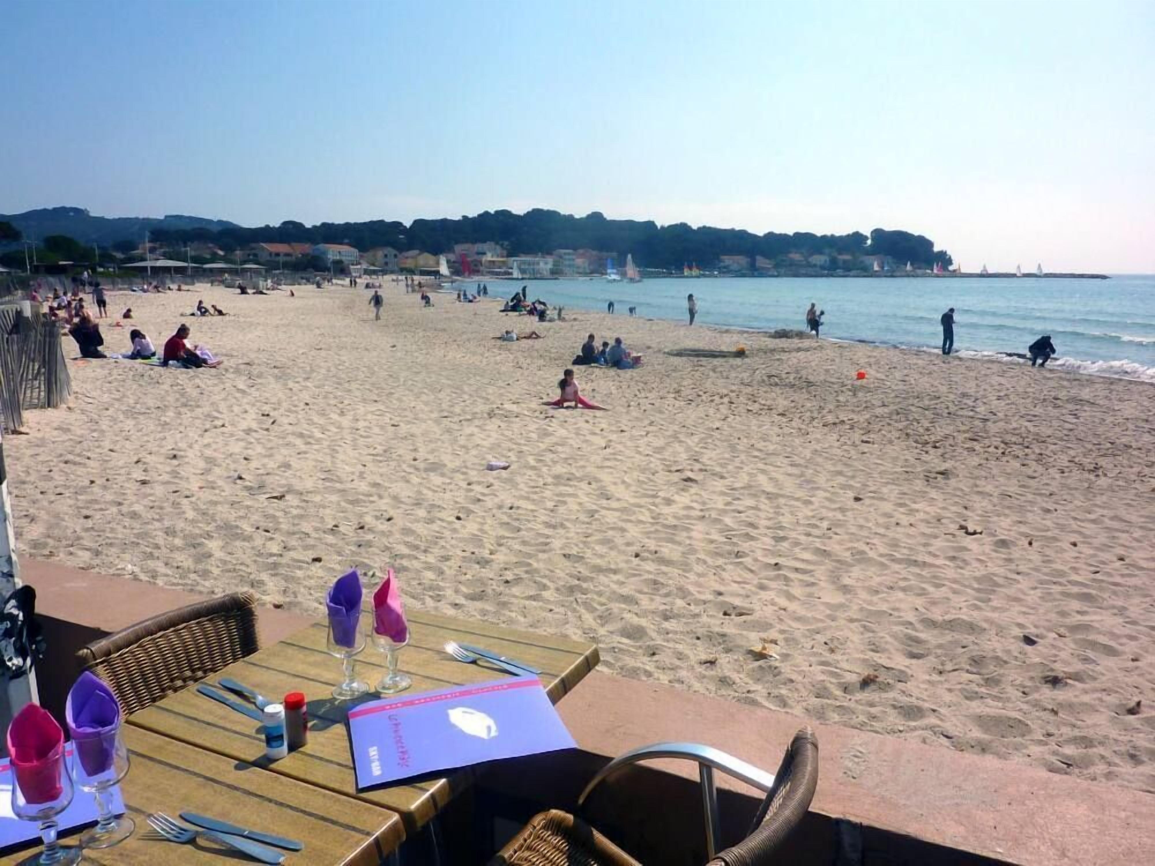 A beachside restaurant with outdoor seating, a view of the beach, and a table set for two.