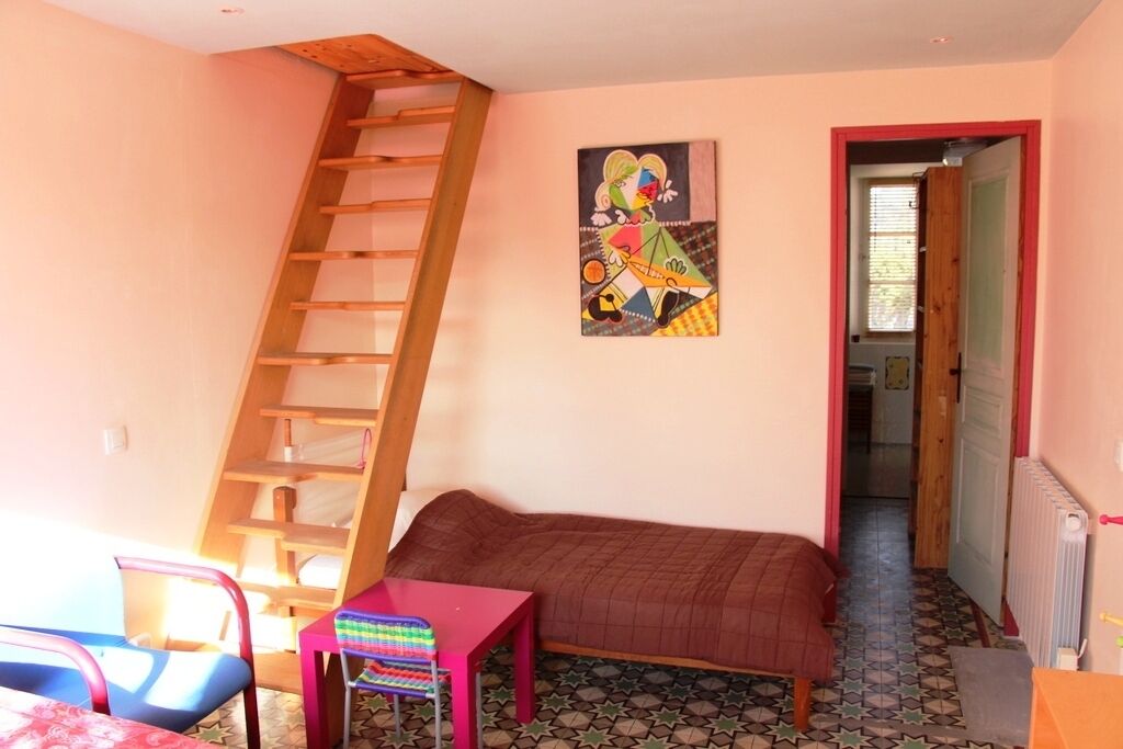 A bedroom with a bunk bed, a wooden ladder, a colorful chair, a small table, and a painting on the wall.