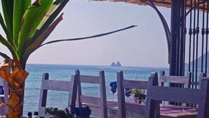 Ein Restaurant direkt am Meer mit Holzkubaturen, einem Tisch mit Topfpflanze und Blick auf das Meer und vorgelagerte Inseln.