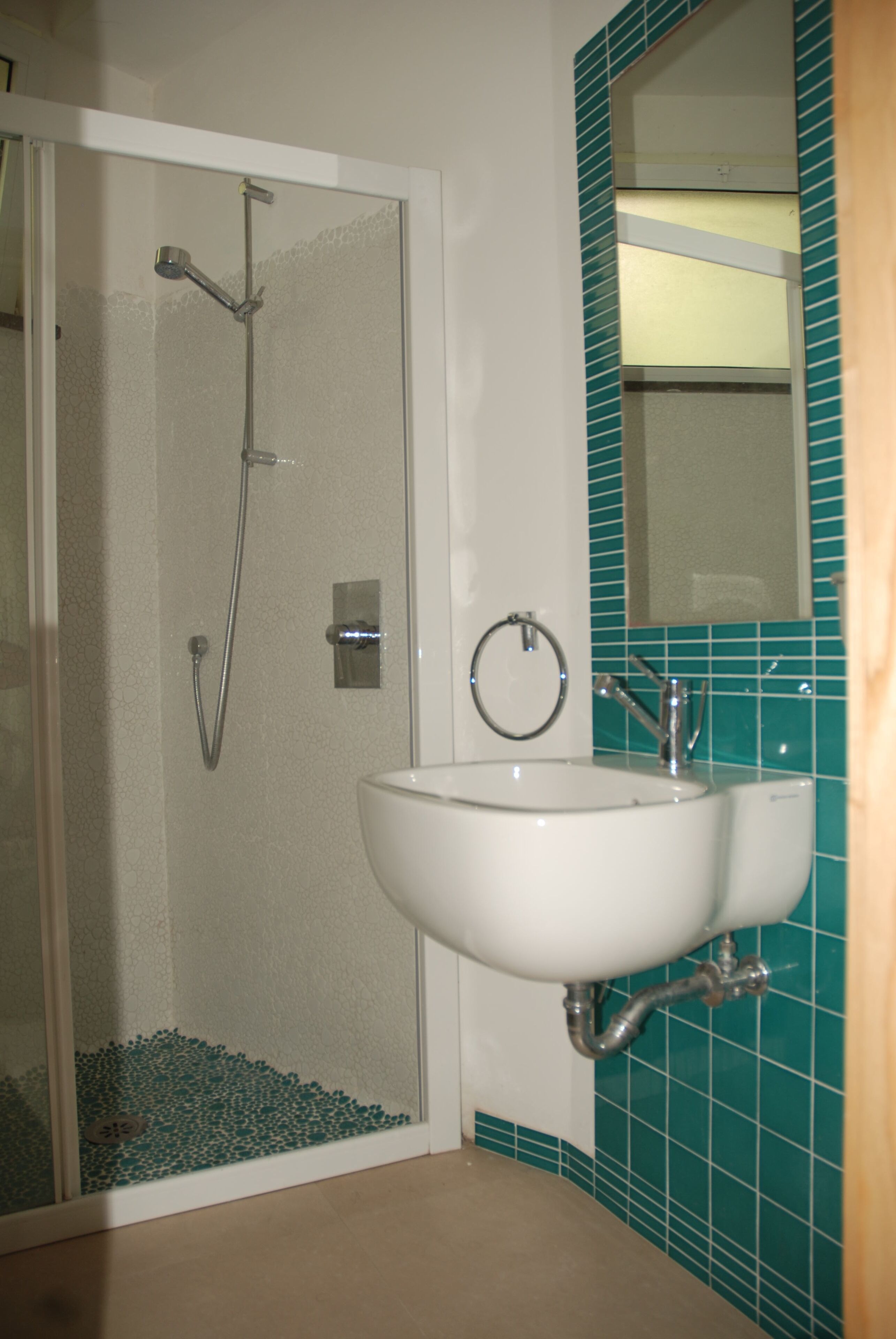 A bathroom with a glass-enclosed shower, a white sink, and a mirror with a teal tile backsplash.