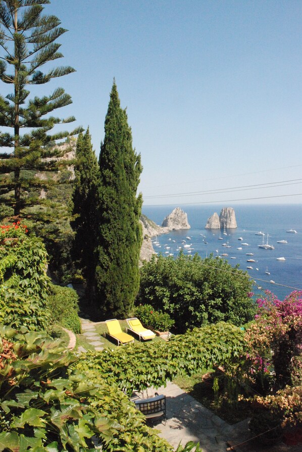 A coastal garden with a pathway leading to a seating area, overlooking the sea and rocky formations.