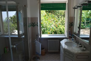 A bathroom with a shower, a sink, and a window with a view of greenery.