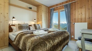 A bedroom with a large bed, wooden walls, a view of mountains, and a window with checkered curtains. - Chalet l'Ange - La Tzoumaz, 4 Vallees (La Tzoumaz)