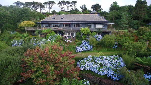 Una casa grande con un jardín amplio, un porche cubierto y vistas a los árboles circundantes.