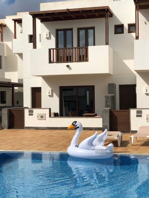 A modern building with a swimming pool, a swan inflatable, and outdoor seating.