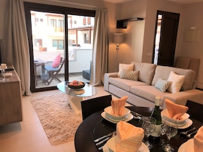 A modern living room with a sofa, a glass coffee table, and a dining table set for a meal.