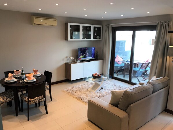 A modern living room with a dining area, a sofa, a TV, and a glass cabinet.