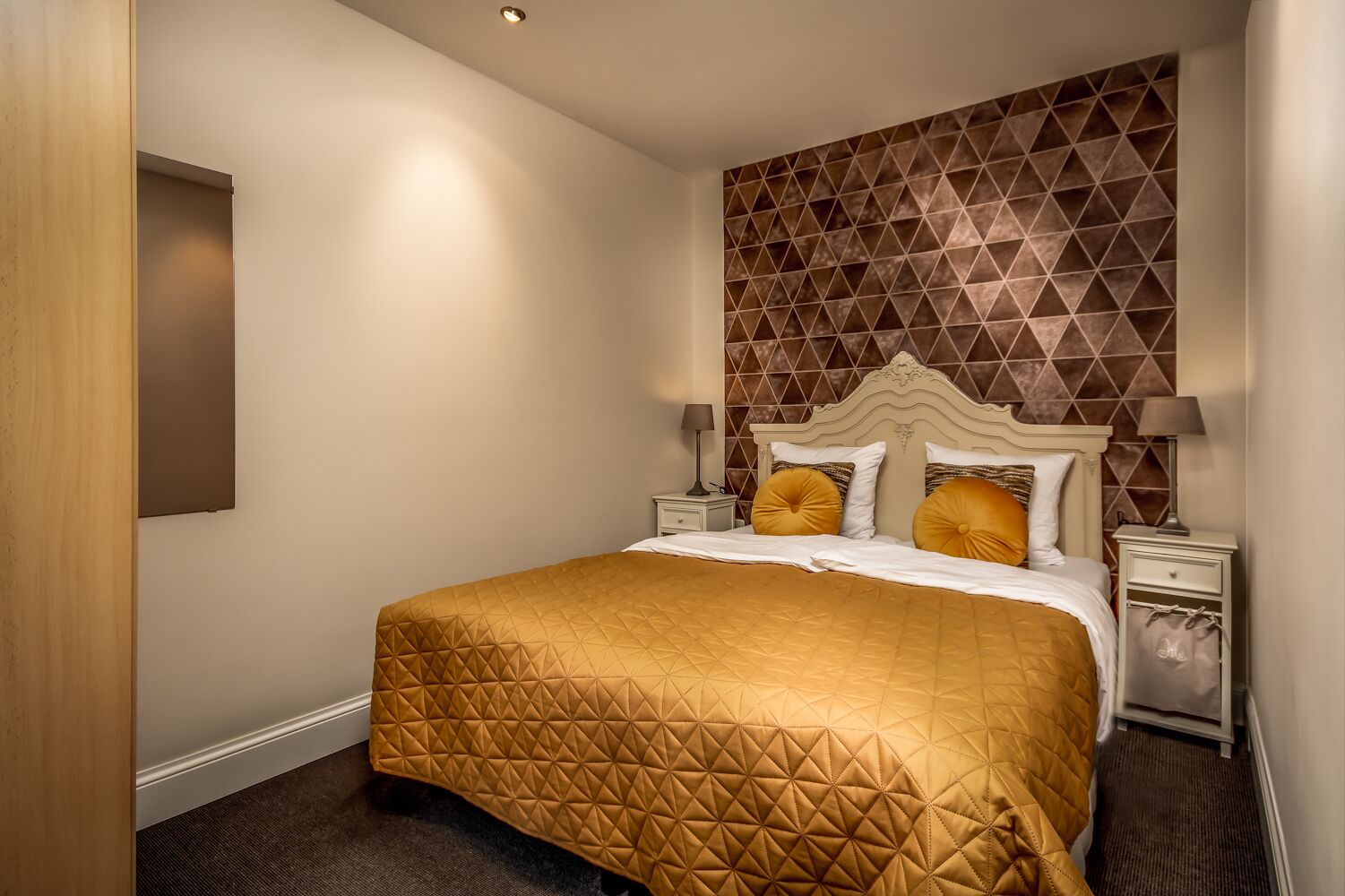A hotel room with a large bed, a geometric-patterned wall, and a wooden door.
