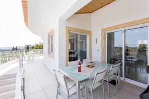 A balcony with a glass table and chairs, a bottle of wine, and a bowl of fruit. - CoolHouses Algarve Lagos | Casa Redonda (Lagos)