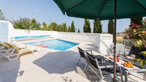 Zona de piscina con sillones, una mesa con comida y bebidas, y vistas al paisaje.