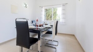 Comedor con una mesa lista para dos personas, sillas, una ventana con cortinas y un aplique de pared.
