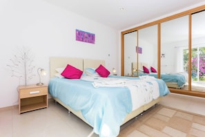 Une chambre à coucher avec un lit, des tables de chevet, un miroir et une vue sur l’extérieur.