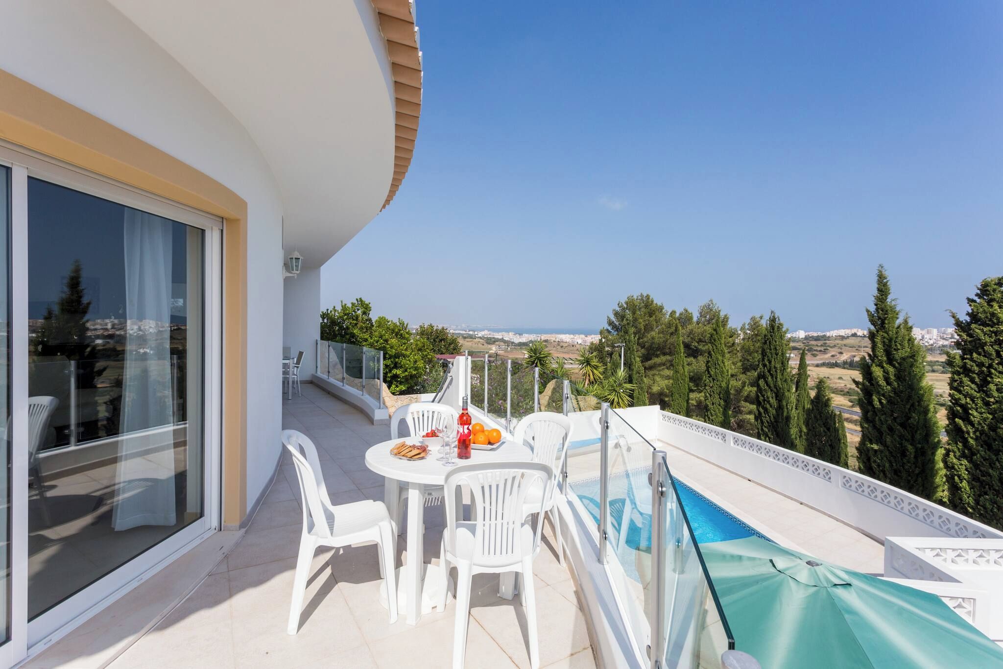 A balcony with a table and chairs, a pool, and a view of the landscape.