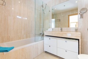 Een moderne badkamer met een glazen douchecabine, een witte wastafel met een marmeren blad en een grote spiegel.