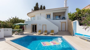Una casa de dos pisos con piscina, mobiliario exterior y una escalera que lleva al piso superior.
