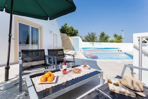Un espace aménagé au bord de la piscine, avec une table dressée pour les repas, un fauteuil de relaxation et une piscine avec des bouées flottantes.