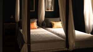 A four-poster canopy bed with two pillows, a bedside table, and a framed picture on the wall.