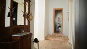 A hallway with a wooden floor, a mirror with a coat rack, and a door leading to a kitchen area.