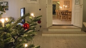 Een gezellige kamer met een kerstboom, een eethoek met een tafel en stoelen, en een muur met ingekaderde foto's.