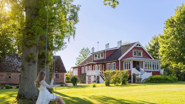 Een rode woning met een witte veranda en een schommel in de voortuin.