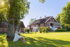 Een rode woning met een witte veranda en een schommel in de voortuin.