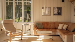 Een gezellige woonkamer met een leren bank, een houten stoel, een klein rond tafeltje en een staande lamp.