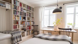 Een knus slaapkamer met een grote boekenkast, een eettafel met stoelen, en een bed met een gebloemd sprei.