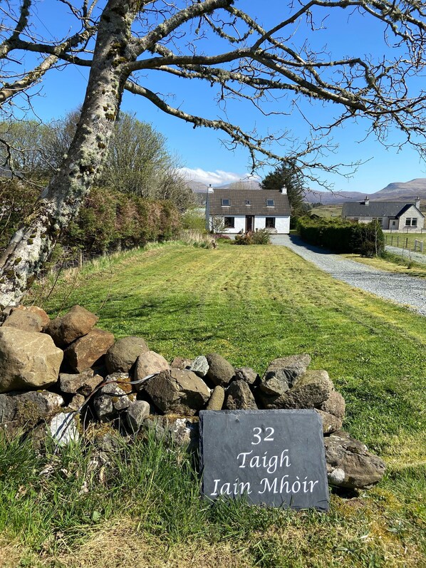 Uma casa de campo com parede de pedra e uma placa com a inscrição '32 Taigh Iain Mhóir'.