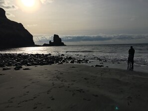 A beach with a rocky shoreline, footprints, and a person standing by the water. - Traditional Croft House with garden.  Ample parking and central location.  (Isle of Skye)