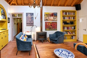 Een gezellige woonkamer met een open haard, een blauwe bank, een houten eettafel en een geel boekenkast vol boeken.
