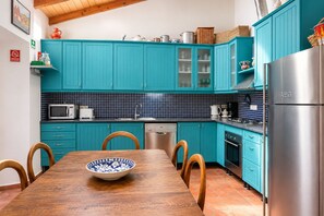 A kitchen with teal cabinets, a wooden dining table, and a stainless steel refrigerator. - Casa Poeta - Charming Town-House in the center of Tavira (Tavira)