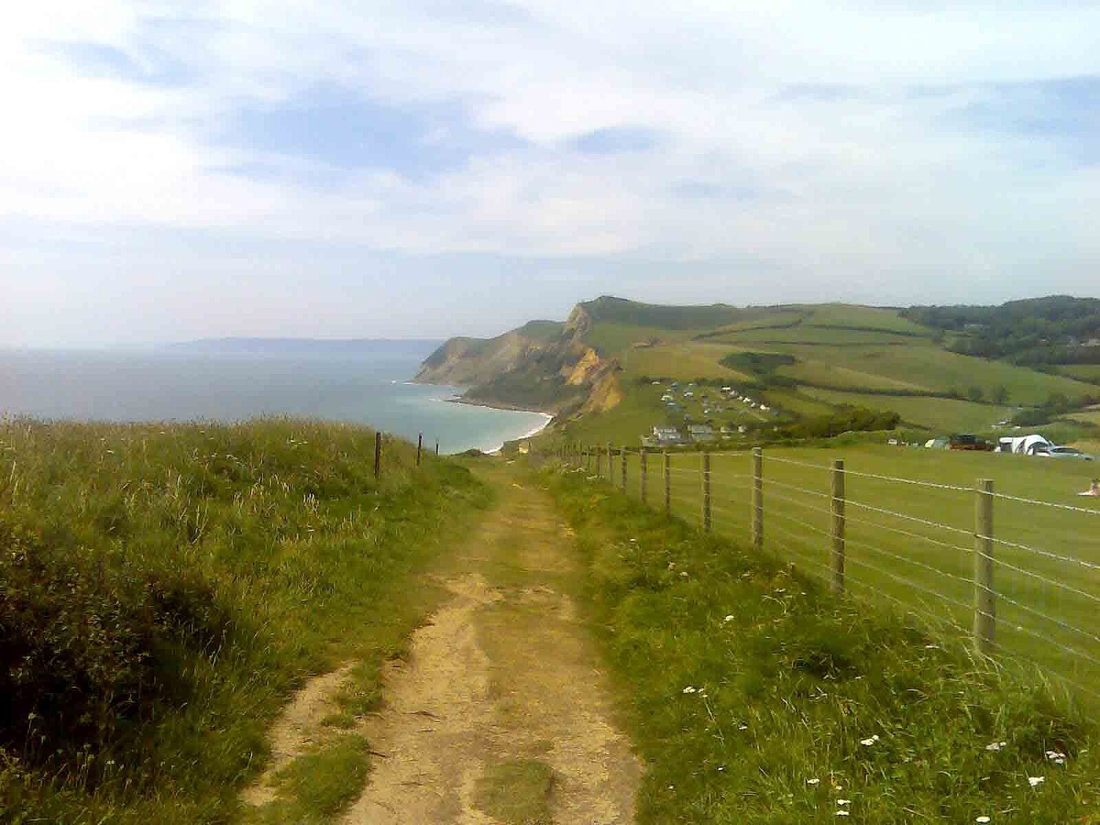 A dirt path leading to a coastal area with houses and a fence.