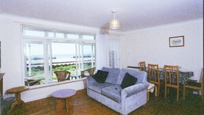 A living room with a large window, a sofa, a dining table with chairs, and a small round table.