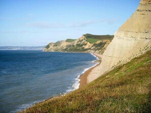 Un paisaje costero con una playa arenosa, acantilados cubiertos de hierba y cielo despejado.