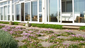 A modern building with large windows and a garden with pink flowers.