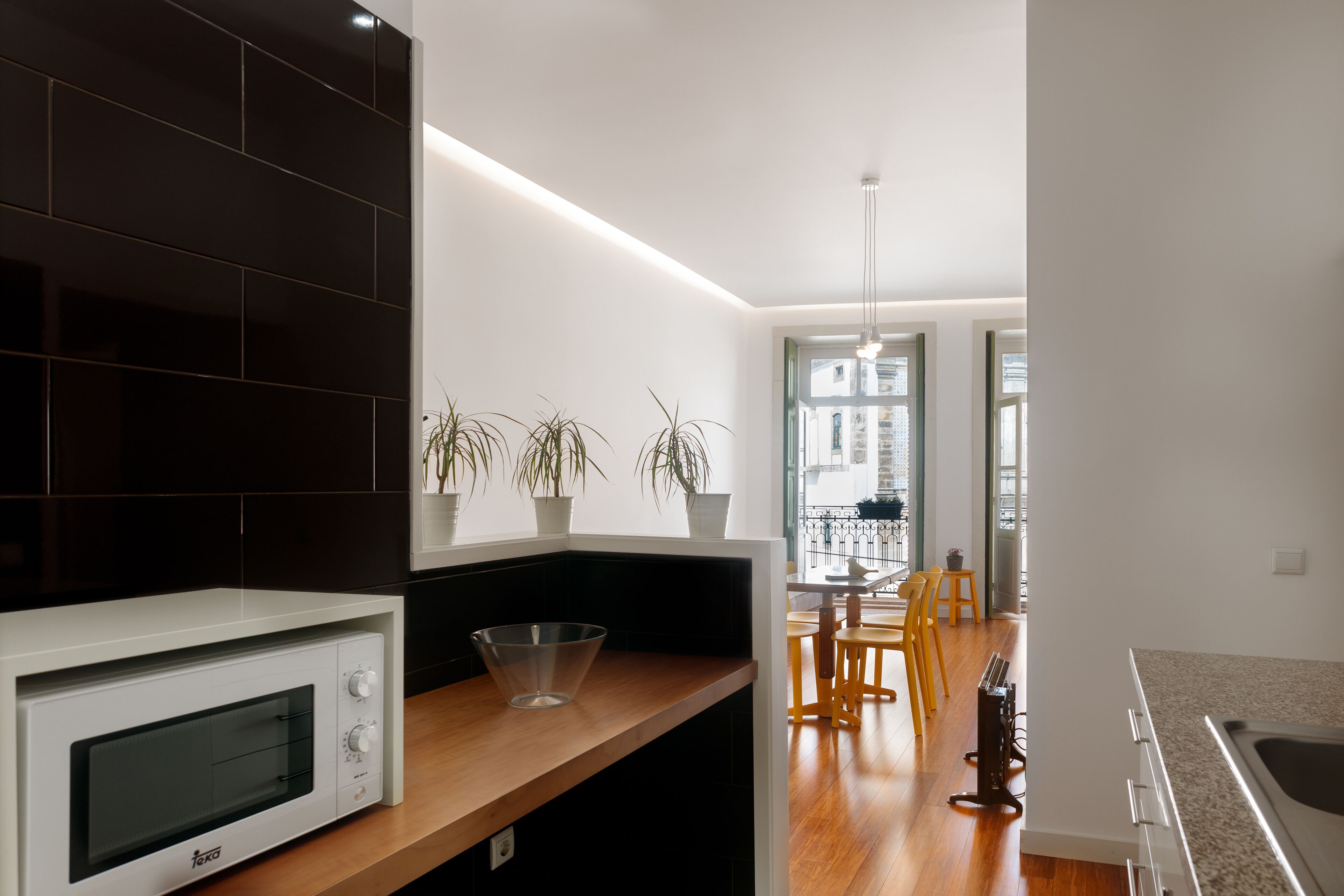 A modern kitchen with a white microwave, wooden countertop, and potted plants.