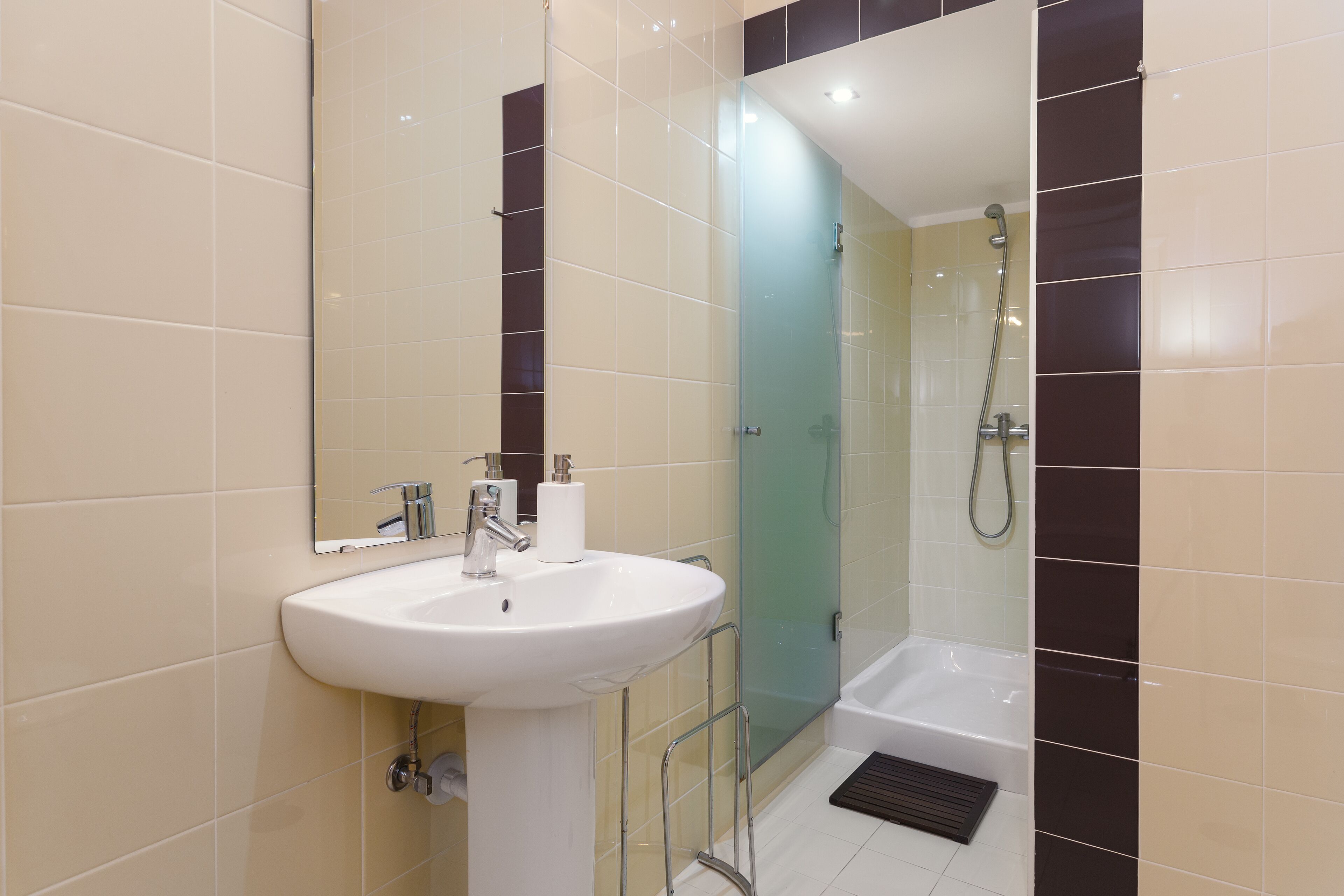 Un baño moderno con lavamanos blanco, espejo y cabina de ducha de vidrio.