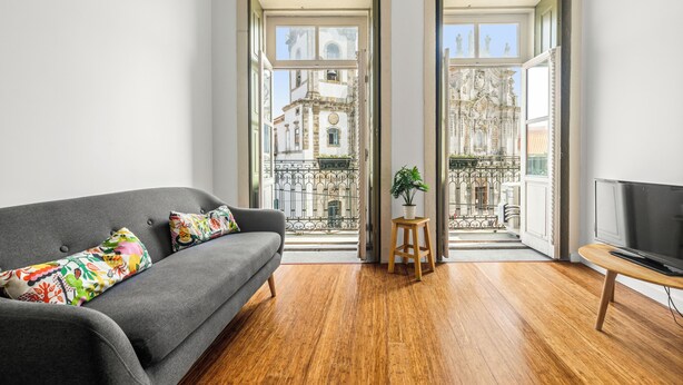Una sala de estar moderna con un sofá gris, cojines coloridos, piso de madera, un mueble para televisor y una planta en maceta.