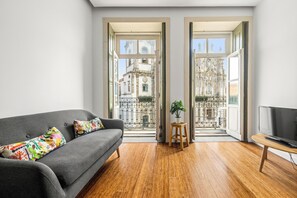 A modern living room with a grey sofa, colorful cushions, a wooden floor, a TV stand, and a potted plant. - The Hungarian Biscuits Apartment  (Porto)