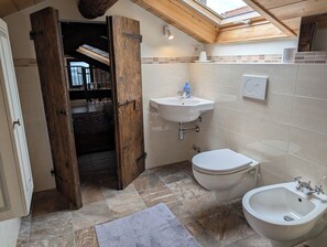 A bathroom with a wooden door, a sink, a toilet, and a bidet.