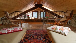 Une chambre mansardée chaleureuse avec un plafond en pente en bois, deux chaises en bois, un tapis à motifs et une vue sur un bâtiment en pierre par la fenêtre.