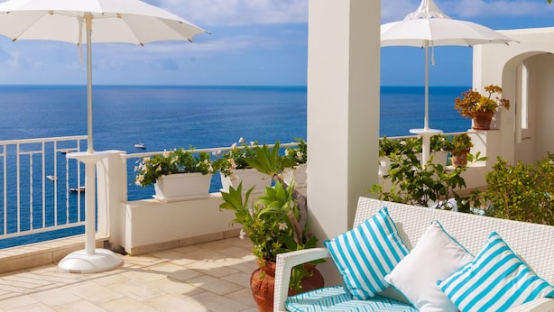 A balcony with white wicker furniture, a white umbrella, and potted plants.