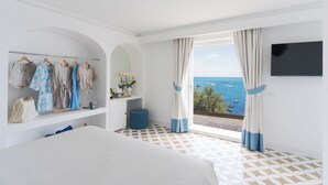 A bedroom with a bed, a wardrobe, a TV, and a balcony with a view of the sea.