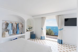 A bedroom with a bed, a wardrobe, a TV, and a balcony with a view of the sea.