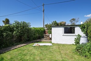 A small white building with a window, surrounded by a grassy yard and dense foliage.