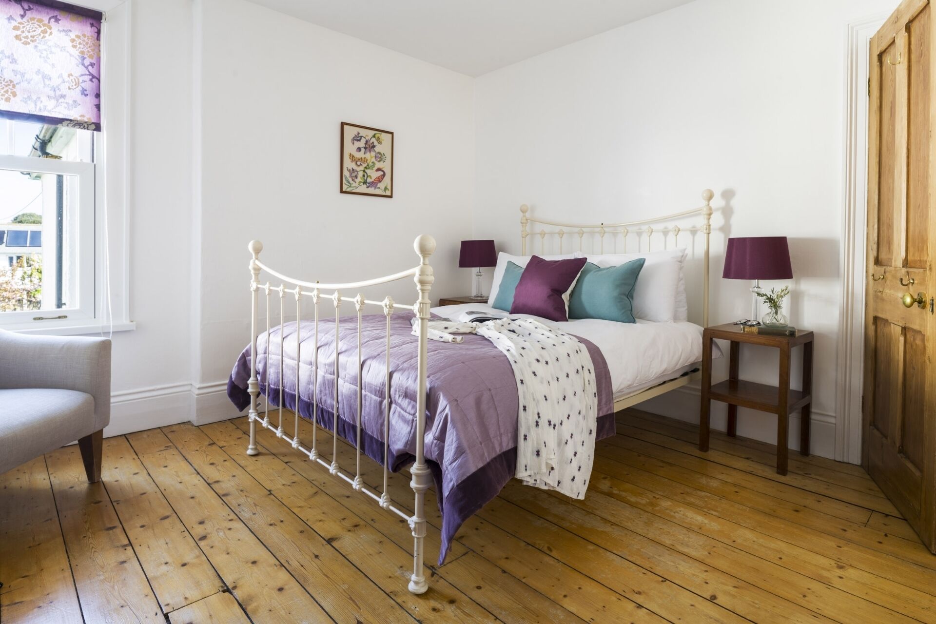 A bedroom with a metal bed frame, a bedside table with a lamp, and a window with a curtain.
